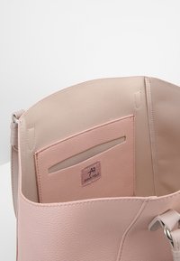 Sac à main en cuir rose clair ouvert pour montrer une poche intérieure pour cartes avec une fenêtre transparente et une étiquette de marque "Anna Field".