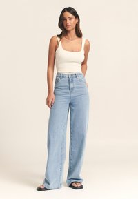 Balta ribota formas bez piedurknēm, gaisīgi zili platajās kājās džinsi ar augstu jostasvietu un melnas dzīvokļveida sandales. Vienkāršs dizains bez redzamām rakstām.