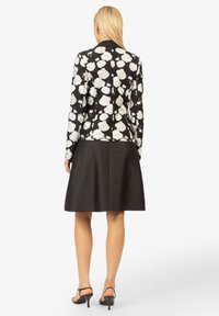 Schwarze Jacke mit weißem Blumenmuster, langen Ärmeln und Kragen, kombiniert mit einem knielangen schwarzen Rock. Glatter Stoff, taillierte Passform.