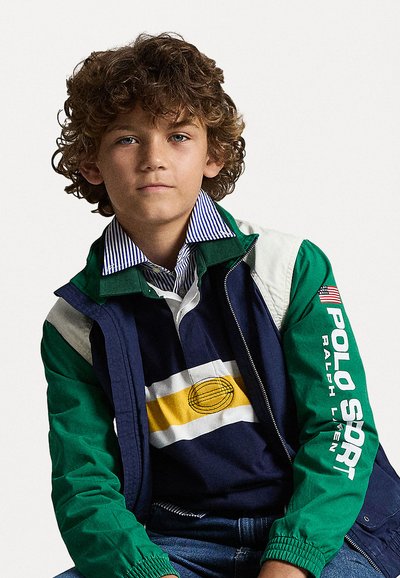 Casaco verde e azul-marinho com detalhes brancos, gola riscada e texto "POLO SPORT". Sobreposto a uma camisa azul-marinho com riscas amarelas e brancas.