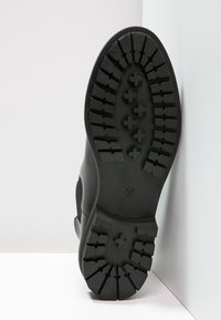 Czarna gumowa podeszwa z głębokim wzorem bieżnika. Detal boczny pokazujący przejście materiału. Rozmiar oznaczony jako 37. Teksturowana dla lepszej przyczepności i stabilności.