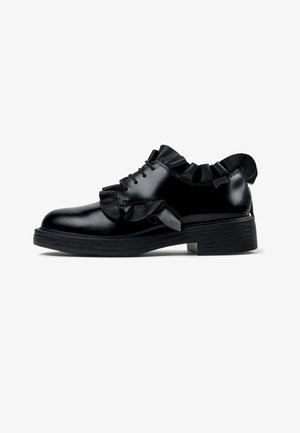 Black patent leather shoe featuring a ruffled accent around the collar, lace-up design, and a low, textured black sole.