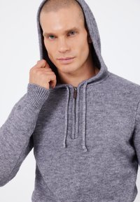 Grauer Strick-Hoodie aus weichem Material, mit einem vorderen Reißverschluss, verstellbarem Kordelzug und gerippten Bündchen. Glatte Textur und lässige Passform.