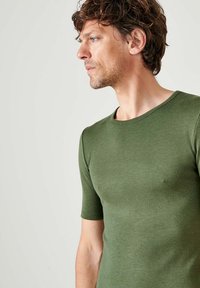 T-shirt attillato a maniche corte in cotone verde scuro. Presenta un collo rotondo e una superficie liscia. Ideale per un look casual.