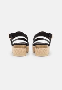 Sandalias negras con tiras, con una plataforma de tacón trenzada en color beige, que cuentan con un detalle de hebilla y un borde de cuerda texturizada en la parte inferior.