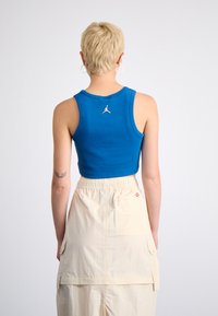 Modrá skrátená tank top s okrúhlym výstrihom a vyšitým logom na zadnej strane, v kombinácii s béžovou, skladanou cargo sukňou s vreckami.