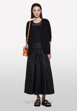 Cardigan nero con bottoni sopra una maglietta trasparente nera, abbinato a una gonna nera arricciata e sandali neri. Accessorio borsa a tracolla arancione.