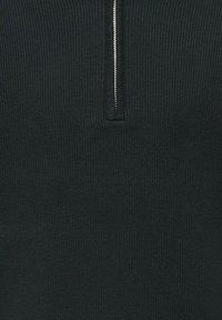 Pull-over noir en tricot côtelé avec un col zippé mi-haut. La texture du tissu est lisse avec des côtes verticales et un détail de fermeture éclair argenté contrastant.