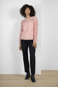 Haut à manches longues en dentelle rose clair avec un motif floral, associé à un pantalon noir à jambes droites et des bottines à talons noirs.