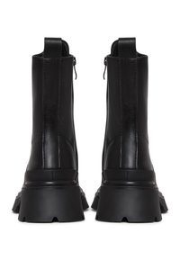 Botas de tobillo negras con un acabado de piel suave, con una suela de goma gruesa y cremallera trasera para facilitar su uso. Diseño minimalista sin patrones visibles.