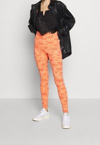 Oranga leggings med ett blommönster, med hög midja och en tight passform, tillsammans med en svart topp och vita sneakers.