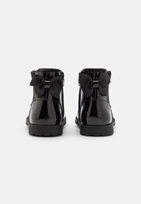 Bottines en cuir verni noir avec un nœud décoratif à l'arrière, finition texturée et semelle texturée pour une meilleure adhérence.