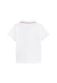 Chemise polo blanche à manches courtes et col, avec un fin accent doré le long du col. Texture de tissu lisse.