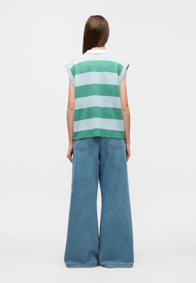 Pull à manches courtes rayé en matière tricotée verte et bleu clair, assorti à un pantalon en denim à jambes larges bleu clair avec poches arrière.