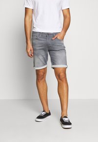 Grå denimshorts med uppvikt fåll, med en klassisk femficksdesign. Bärs med en enkel vit T-shirt och svarta sneakers.