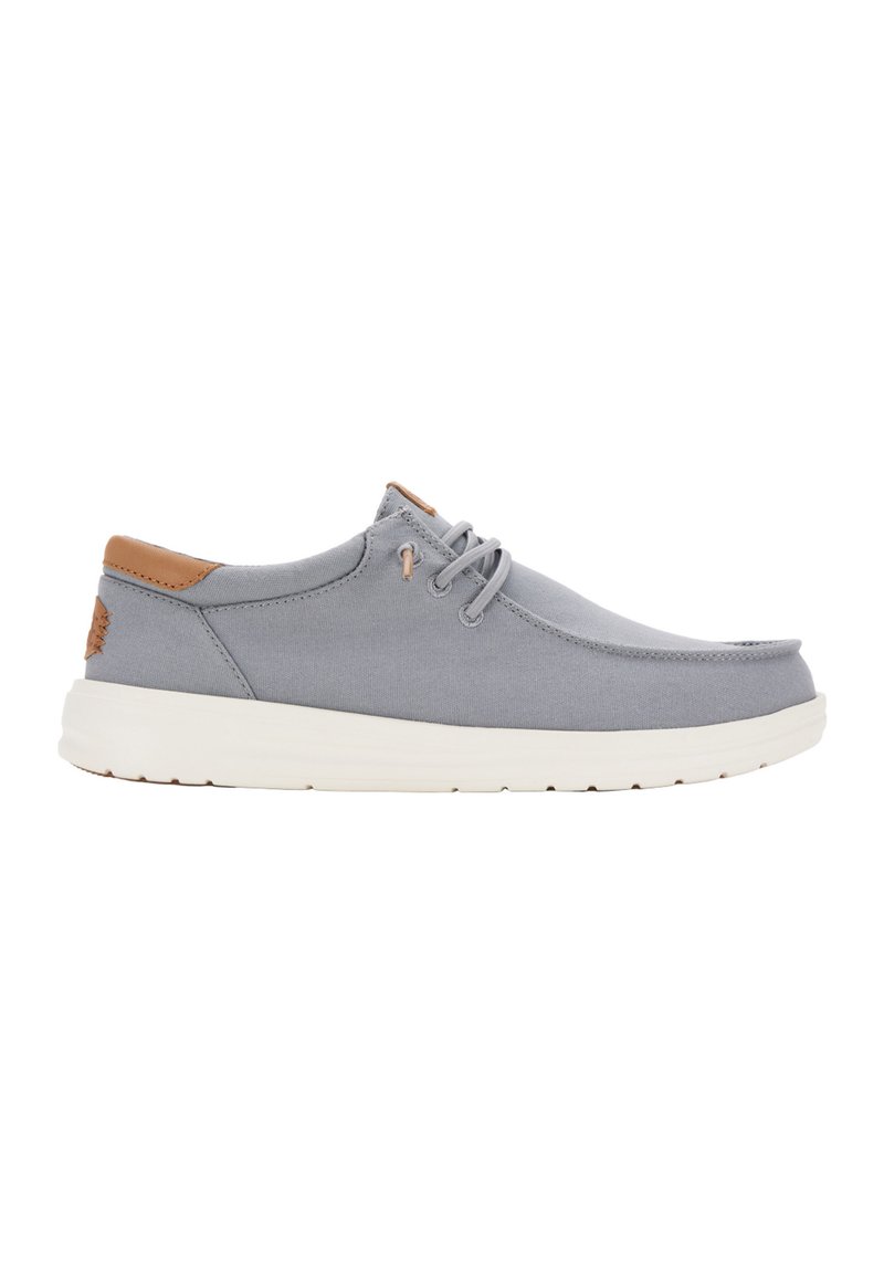 Zapato de lona gris con punta redonda, detalles en cuero marrón y suela ligeramente acolchada. Presenta cordones y una parte superior texturizada.