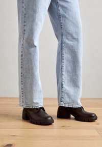 Zapatos de tacón negros con suelas de goma, que presentan una textura suave y punta redondeada, combinados con jeans rectos de color azul claro.