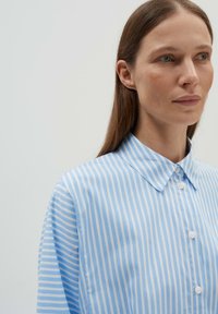 Hellblaues Button-Down-Hemd mit weißen horizontalen Streifen, besitzt einen spitzen Kragen und eine glatte Textur. Weiches Material mit klassischem Design.