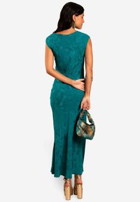 Cyan bloemenprint maxi-jurk met een getailleerde silhouet, korte mouwen en een lichte flare aan de zoom. Gecombineerd met een gestructureerde handtas.