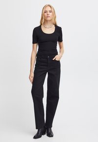Top negro de manga corta con escote en forma de corazón, combinado con pantalones negros de cintura alta. La modelo lleva botas de tobillo negras con tacón y un collar.