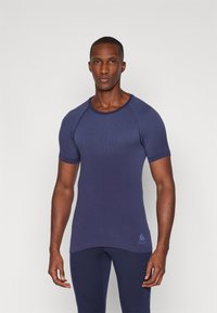 Kortermet, crew-neck treningsskjorte laget av teksturert marineblått stoff, med et subtilt gradientmønster og en logo på den nedre siden.