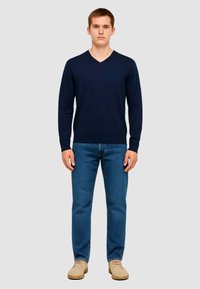 Maglione a collo a V blu navy realizzato in materiale morbido, indossato con jeans blu e scarpe color cammello. Vestibilità slim, maniche lunghe e polsini e orlo a costine.