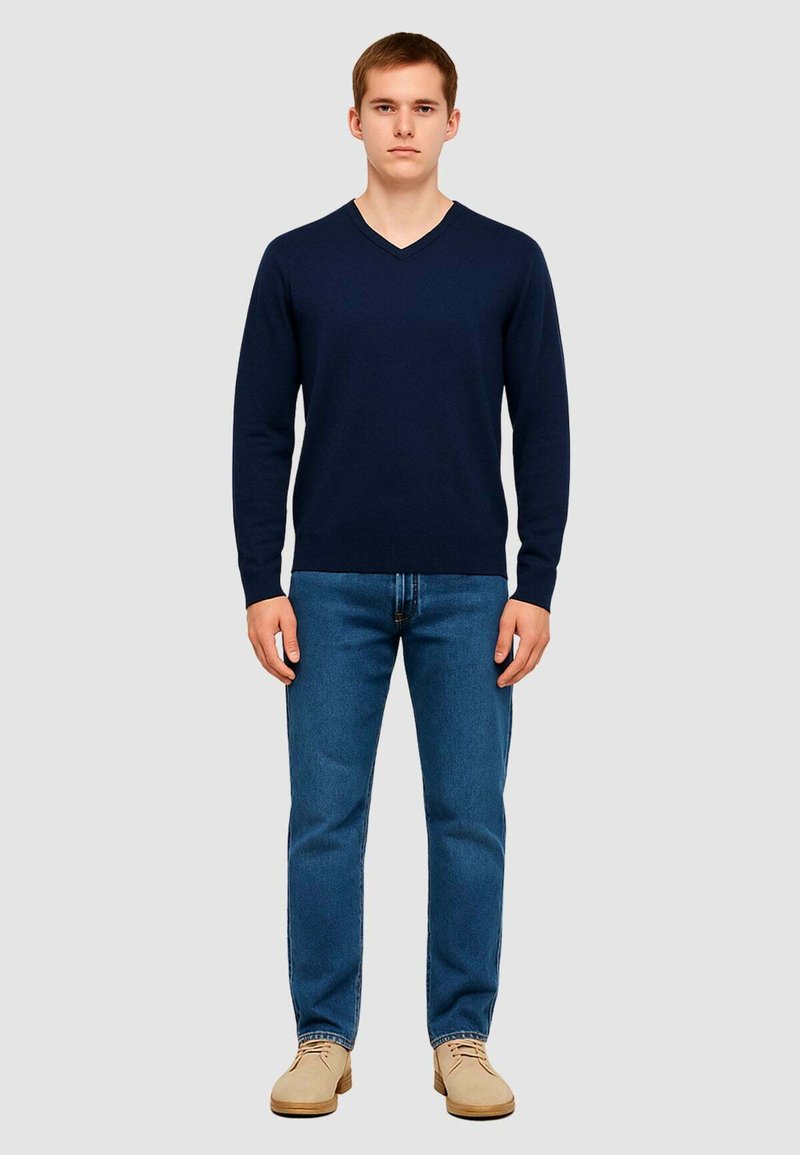 Maglione a collo a V blu navy realizzato in materiale morbido, indossato con jeans blu e scarpe color cammello. Vestibilità slim, maniche lunghe e polsini e orlo a costine.