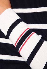 Laivastonsininen ja valkoinen raidallinen neulepaita, jossa on resoritekstuuri. Hihansuut ovat vuorotellen laivastonsinisiä, valkoisia ja kapealla punaisella korostuksella.