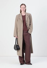 Long beige striped coat with a classic collar, brown fitted top, and wide brown pants, paired with a small black handbag and pointed shoes.