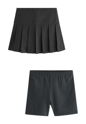 Junges Mädchen, das eine weiße langärmelige Bluse, einen dunkelgrauen plissierten Rock, weiße kniehohe gemusterte Socken und schwarze Riemenschuhe trägt.