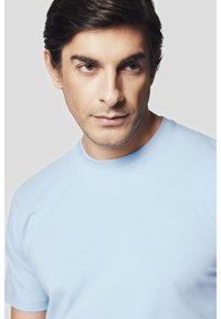 Jasnoniebieska koszulka typu crew-neck wykonana z bawełny, o gładkiej fakturze i krótkich rękawach. Brak widocznych wzorów lub akcentów.