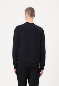 Sudadera negra hecha de una tela suave, con un cuello redondo clásico y puños acanalados, de corte relajado y sin logotipos visibles.