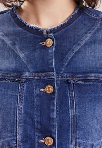 Jeansjacka med fransiga kanter, bronserade knappar och detaljerad sömnad. Har framfickor och en strukturerad design i mörkblå.