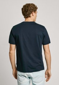 Camiseta de algodón azul marino con mangas cortas, escote redondo y una textura suave. Presenta un pequeño detalle del logo en la parte posterior.
