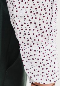 Biała koszula z kwiatowym wzorem w czerwone i niebieskie, z zapięciem na guzik i gładką teksturą tkaniny.