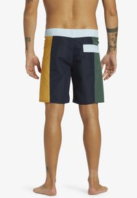 Bunte Badeshorts mit einem Design, das Paneele in Marineblau, Gelb, Grün und Hellblau zeigt. Mit einer hinteren Tasche und einer glatten Textur.