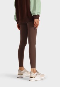 Leggings marroni realizzati in materiale elastico, abbinati a sneakers chiare con accenti metallici. La parte superiore ha maniche a sbuffo e un corpo marrone.