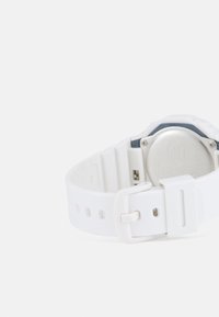 Bracelet de montre en caoutchouc blanc avec un fond de boîtier métallique argenté, présentant des détails circulaires et une fermeture à boucle. Texture lisse, design minimaliste.