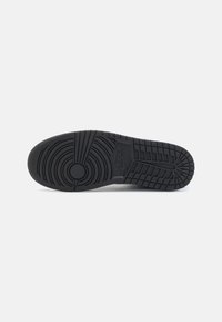 Mustat kumiset sneaker-pohjat, joissa on pyöreitä ja lineaarisia kuvioita. Ominaisuuksina erottuva logo ja teksturoitu pinta pidon parantamiseksi.