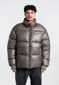 Rudas pūkinis švarkas su aukšta apykakle, siūtomis dalimis ir pilkais megztiniais rankogaliais. Yra priekinis užtrauktukas ir logotipas ant krūtinės.