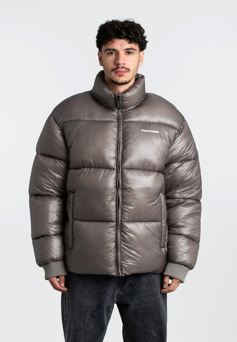 Rudas pūkinis švarkas su aukšta apykakle, siūtomis dalimis ir pilkais megztiniais rankogaliais. Yra priekinis užtrauktukas ir logotipas ant krūtinės.