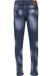 Vue arrière d’un jean slim bleu en denim avec des détails délavés et usés et deux poches arrière, doté d’un patch de marque en cuir marron.