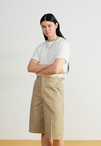 Khaki shorts with a straight cut and pleats, paired with a fitted white t-shirt. Features a small logo on the waistband.