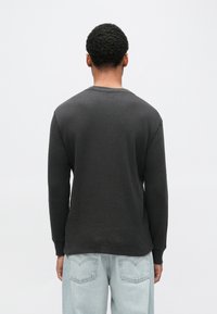 Sötétszürke bordázott hosszú ujjú póló kerek nyakkal, texturált anyaggal és laza szabással, világoskék farmerrel viselve.