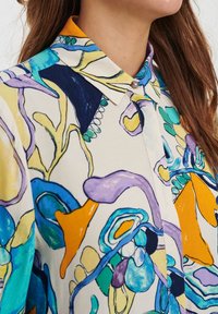 Blusa multicolor con un patrón floral y abstracto, fabricada con un tejido ligero, con collar en punta y detalle de botones.