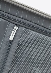 Gray suitcase interior with two zippered compartments, one solid fabric and one mesh, both featuring silver metal zippers.