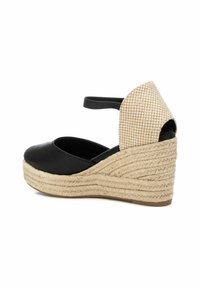Sandalia de cuña de cuero negro con una correa de tobillo trenzada en beige y una suela envuelta en yute, que presenta una puntera redondeada y detalles texturizados.