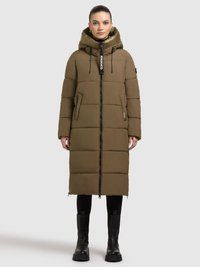 Lange groene pufferjas met capuchon, voorzien van een rits aan de voorkant, zijzakken en elastische manchetten. Gestyled met zwarte legging en stevige laarzen.