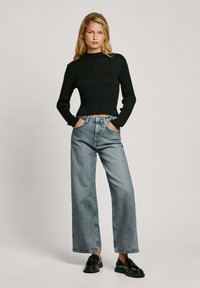 Svart ribbad cropptröja kombinerad med ljusblå vida jeans. Outfiten inkluderar svarta loafers med gyllene detaljer. Enkelt, modernt design.