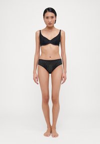 Melnā mežģīņu bralette un atbilstošas apakšbikses ar ziedu rakstu, viļņotām malām un gludu tekstūru. Izstrādāts, lai veidotu pieguļošu siluetu.